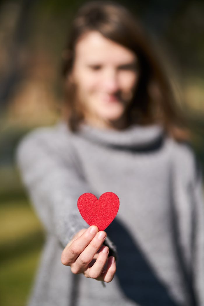 A woman presenting a red heart symbol, showcasing love and compassion.